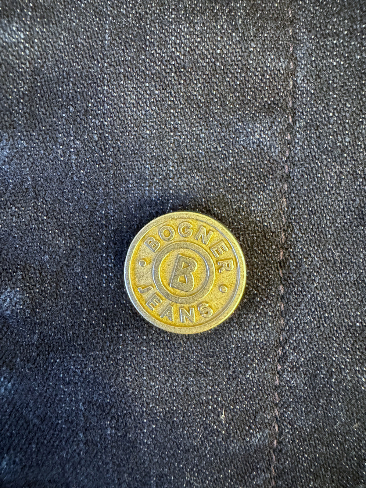 Brandsamsara Bogner Jeans jacket featuring a gold-toned metal button with embossed branding on dark blue denim fabric.