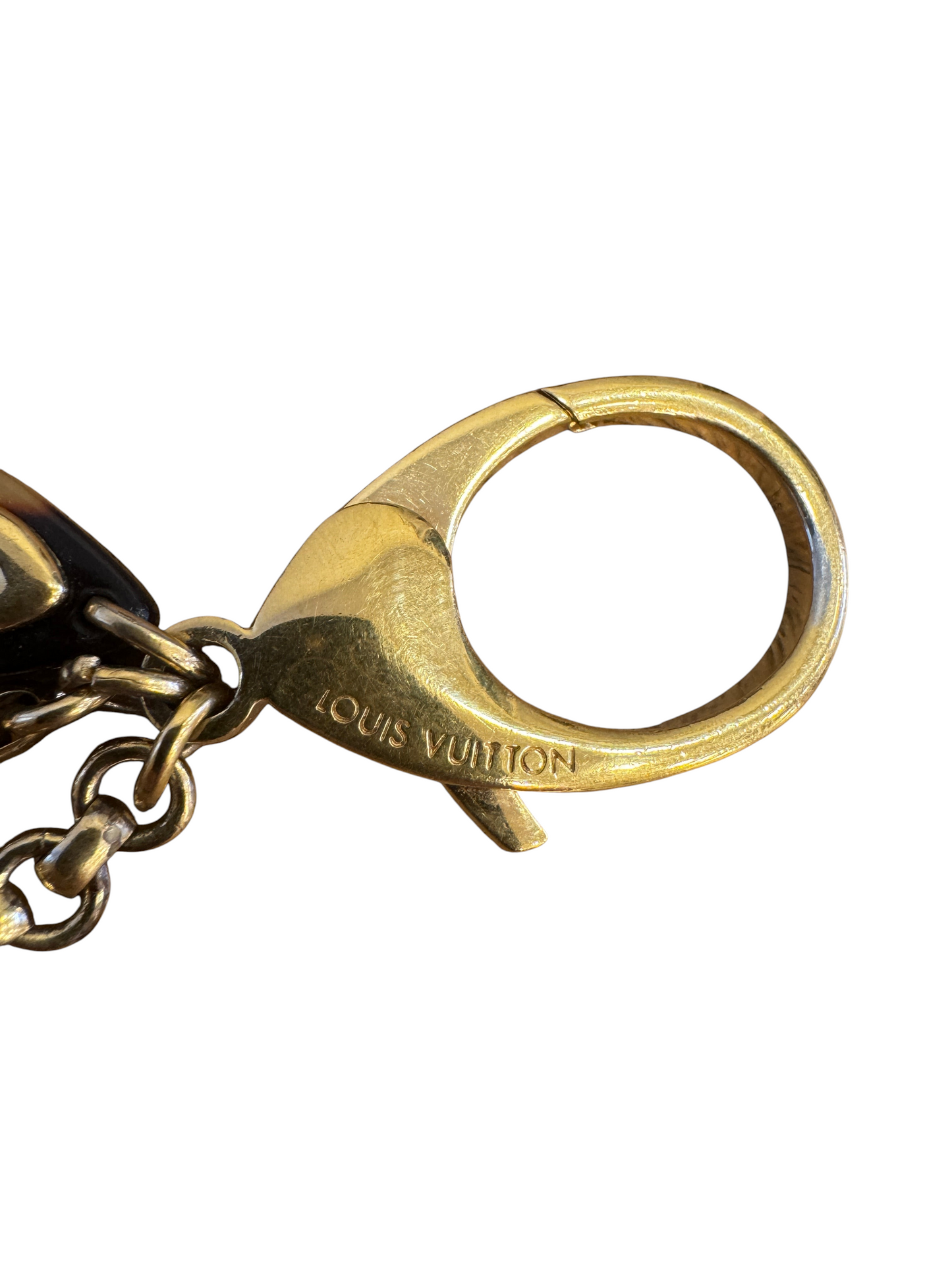 Brandsamsara Louis Vuitton Bijoux Sac Insolence bag charm featuring a polished gold-tone brass clasp on wood surface