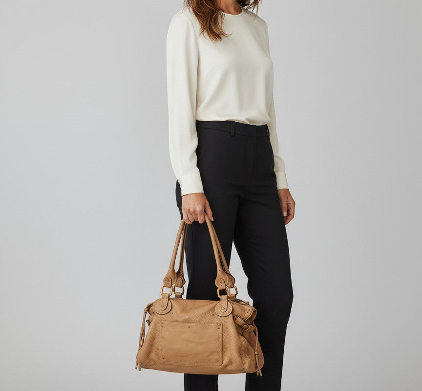 Brandsamsara tan pebbled leather satchel bag with double handles and gold hardware. Features a front pocket and decorative studs.